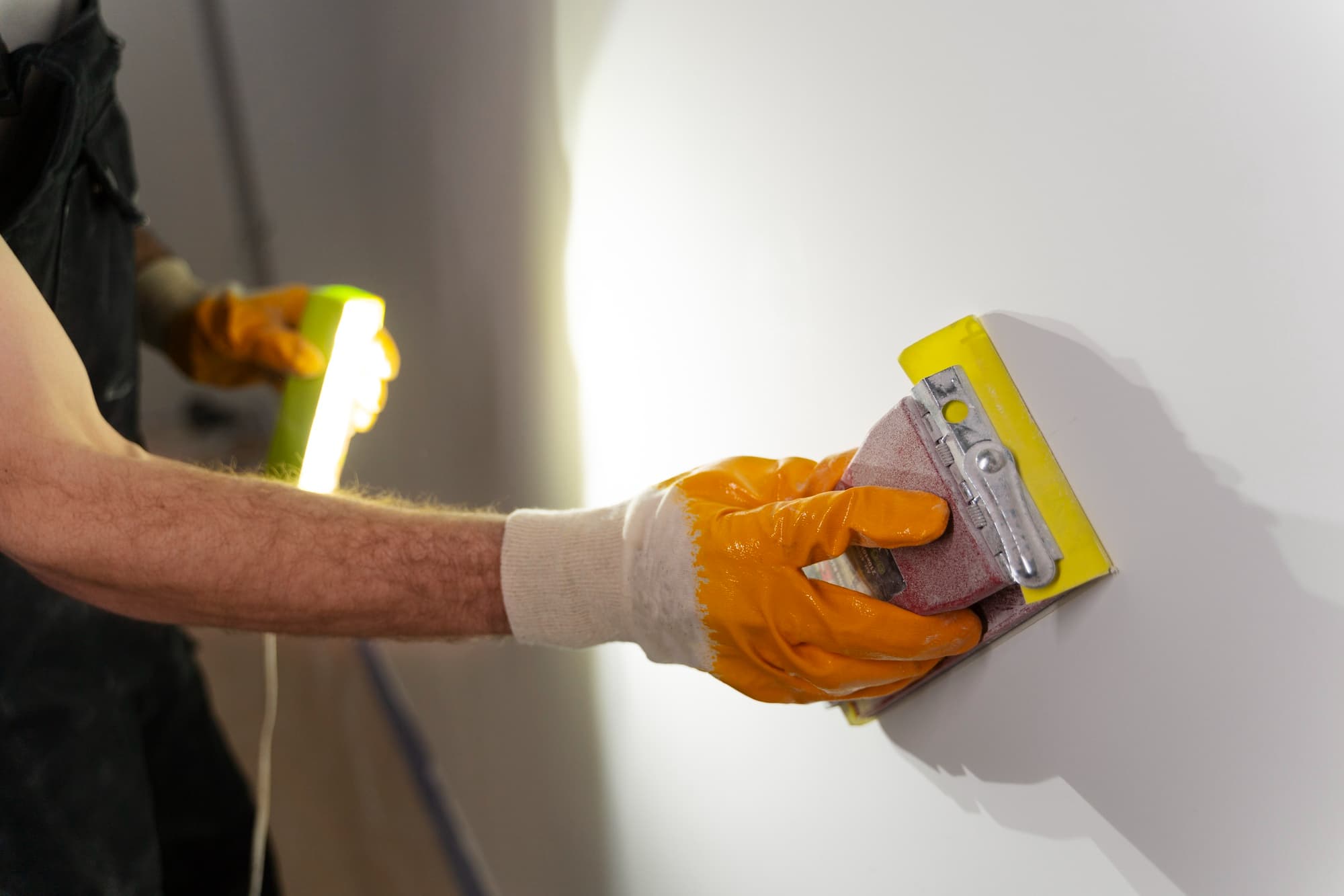 Maler schleift eine gespachtelte Wand im Streiflicht mit dem Handschleifer